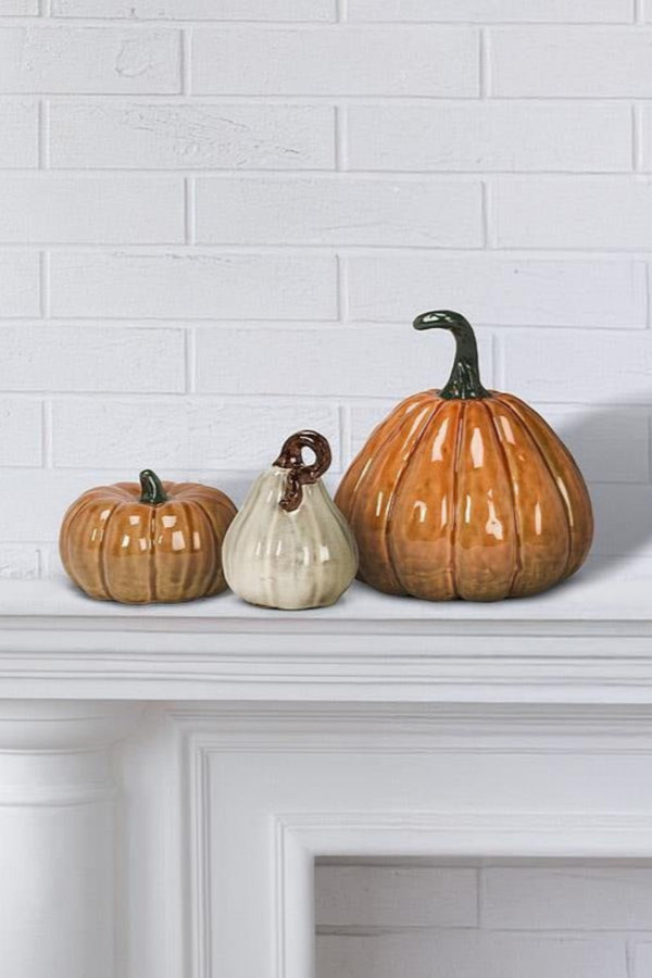 Three ceramic pumpkins on a white fireplace mantle against a white brick wall.
