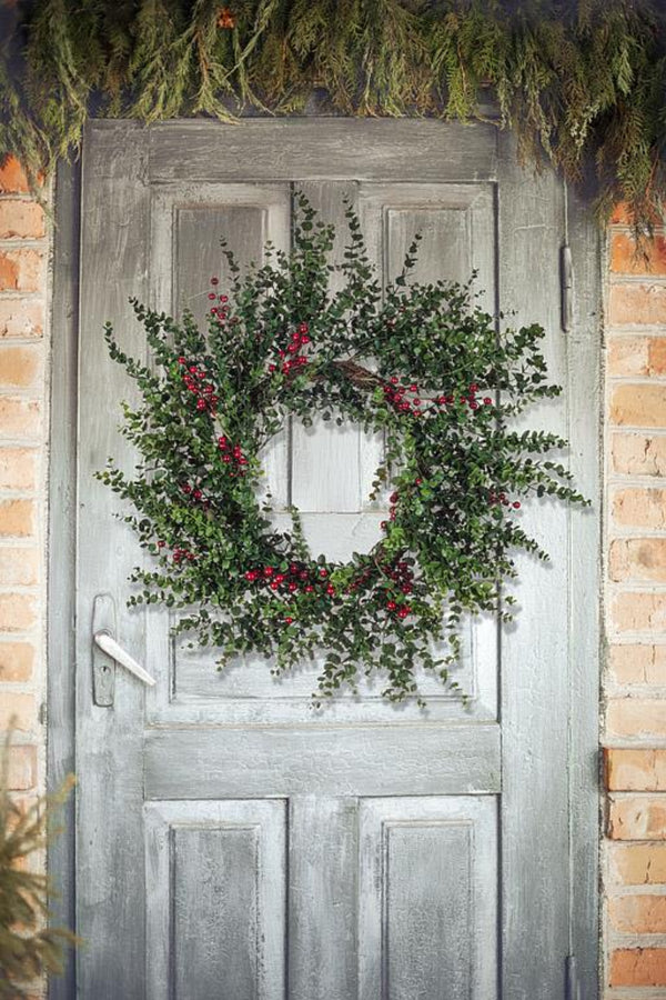 Decorative wreath with greenery and red berries on a wooden door with a brick background