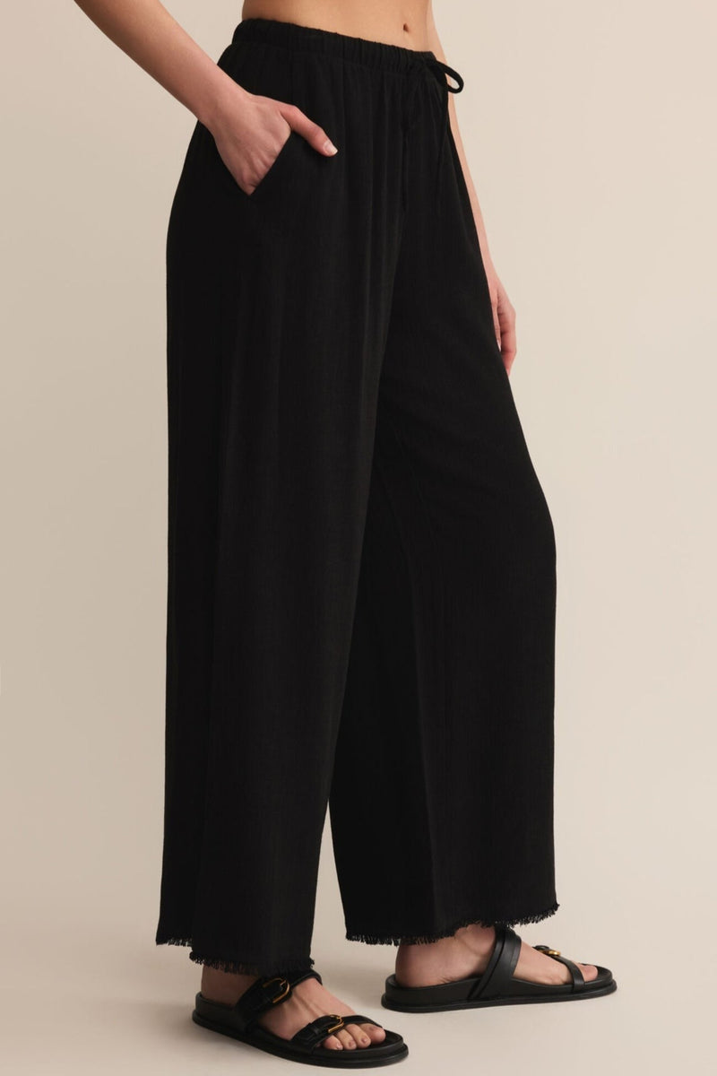 Person wearing black wide-leg pants on a beige background