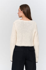 Woman wearing a textured white sweater and black pants on a light gray background