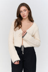 Woman wearing a cream-colored textured cardigan over a black top on a light gray background