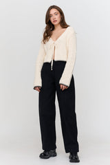 Woman wearing a cream cardigan, black pants, and black shoes on a white background