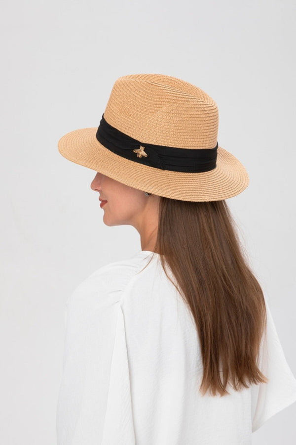 Woman wearing a beige hat with a black band on a light gray background