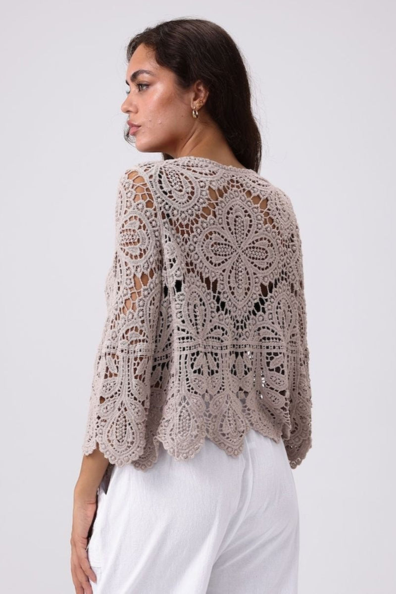 Woman wearing a beige crochet shrug against a white background