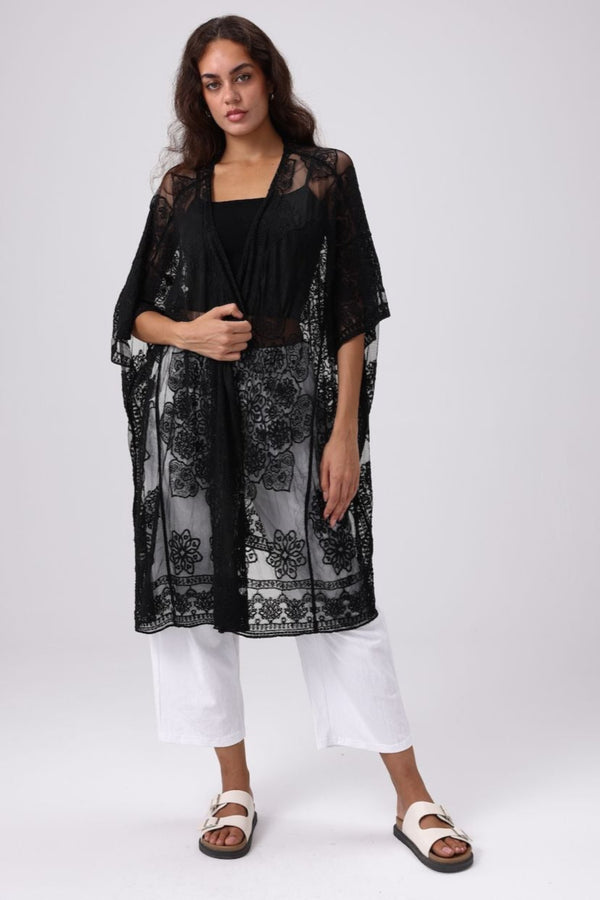 Woman wearing a black floral kimono over a black top and white pants on a white background
