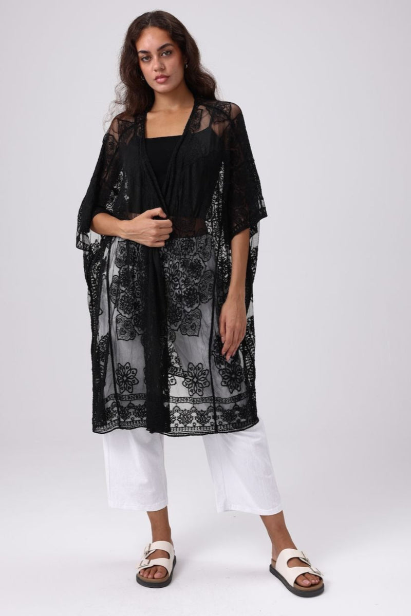 Woman wearing a black floral kimono over a black top and white pants on a white background