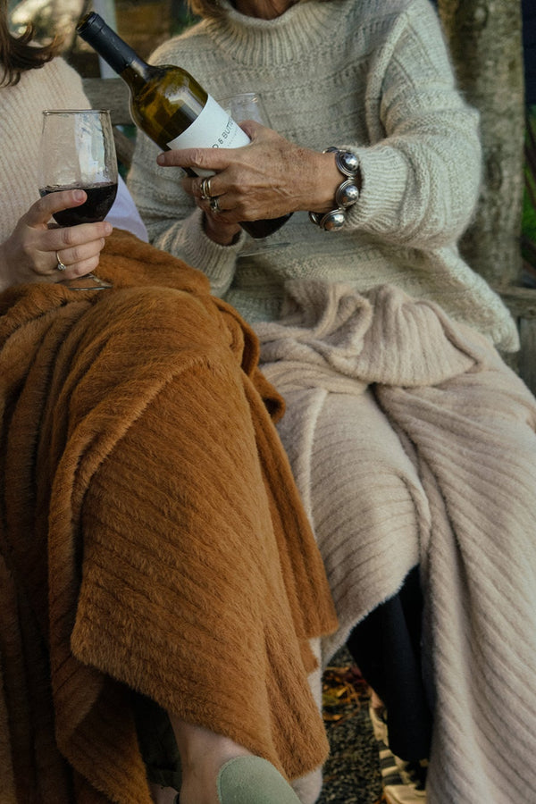 Two people sitting on a bench with wine bottles, wrapped in blankets.
