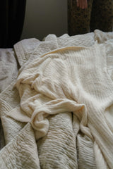 Beige textured blanket on a bed with a person partially visible in the background.