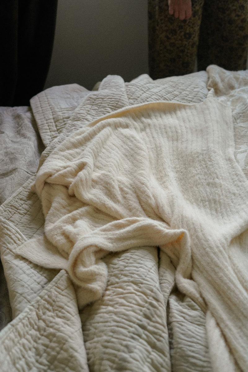 Beige textured blanket on a bed with a person partially visible in the background.