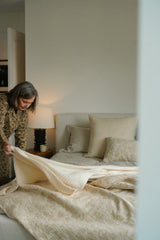 Woman making the bed in a bedroom with neutral tones.