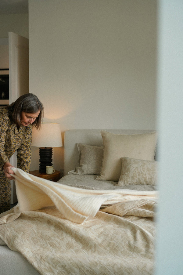 Woman making the bed in a bedroom with neutral tones.