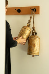 Person holding two vintage-style brass bells against a neutral wall.