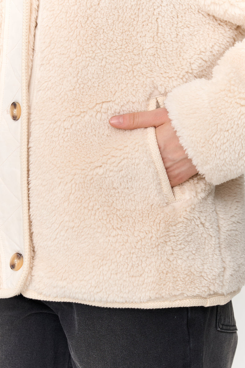 Close-up of a person wearing a cream sherpa jacket with a neutral background