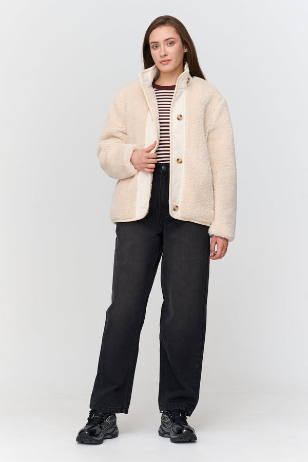 Woman wearing a beige jacket, striped shirt, and black pants on a white background