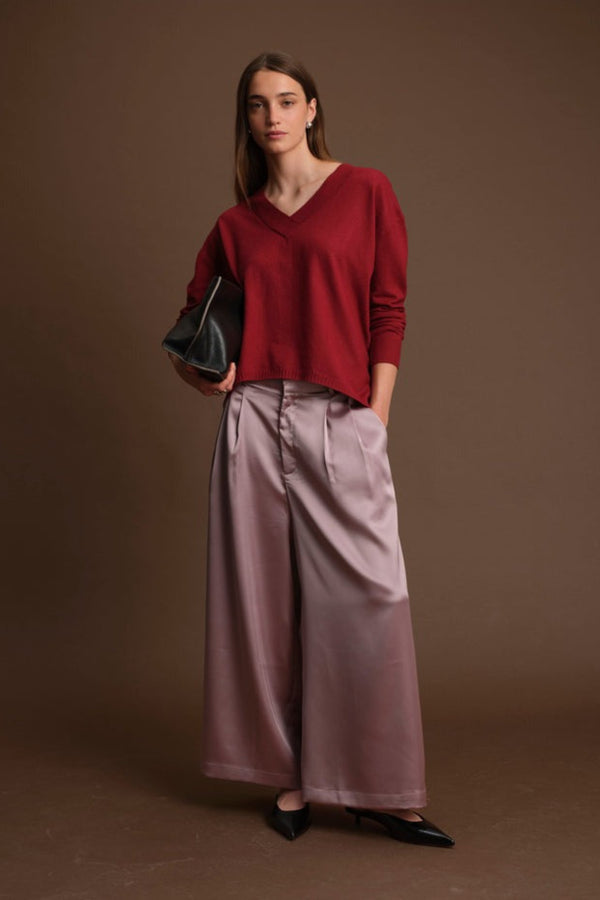 Woman wearing a red sweater and pink pants against a brown background