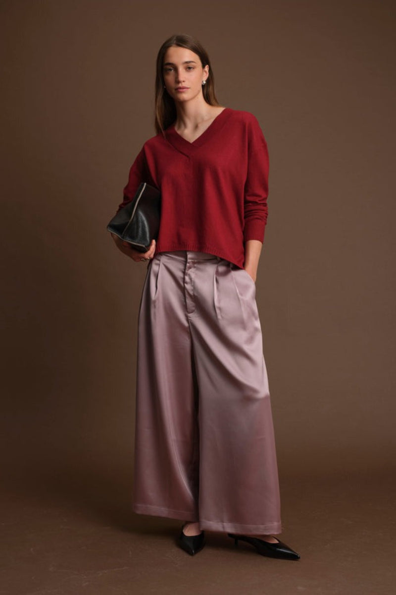 Woman wearing a red sweater and pink pants against a brown background