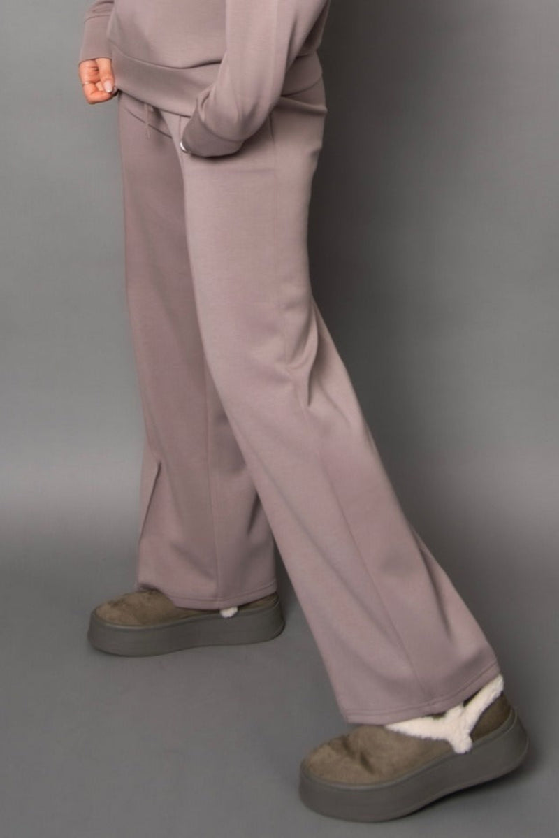 Person wearing a light grey/beige  tracksuit with wide-leg pants on a gray background