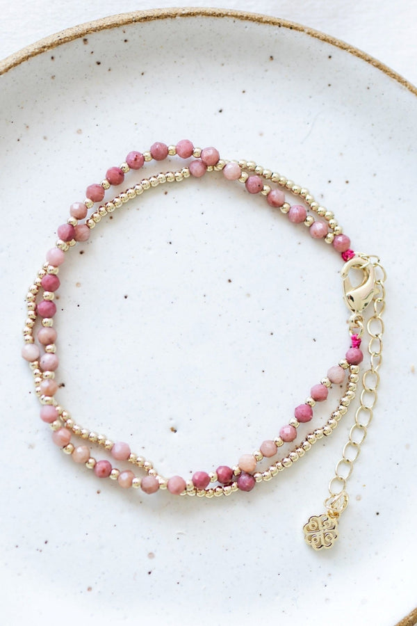 Pink beaded bracelet with gold chain on a textured white surface