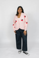 Person wearing a pink cardigan with cherry designs on a white background