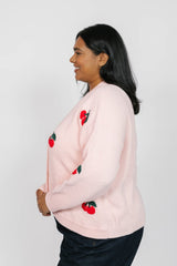 Woman wearing a light pink sweater with red cherry designs on a white background
