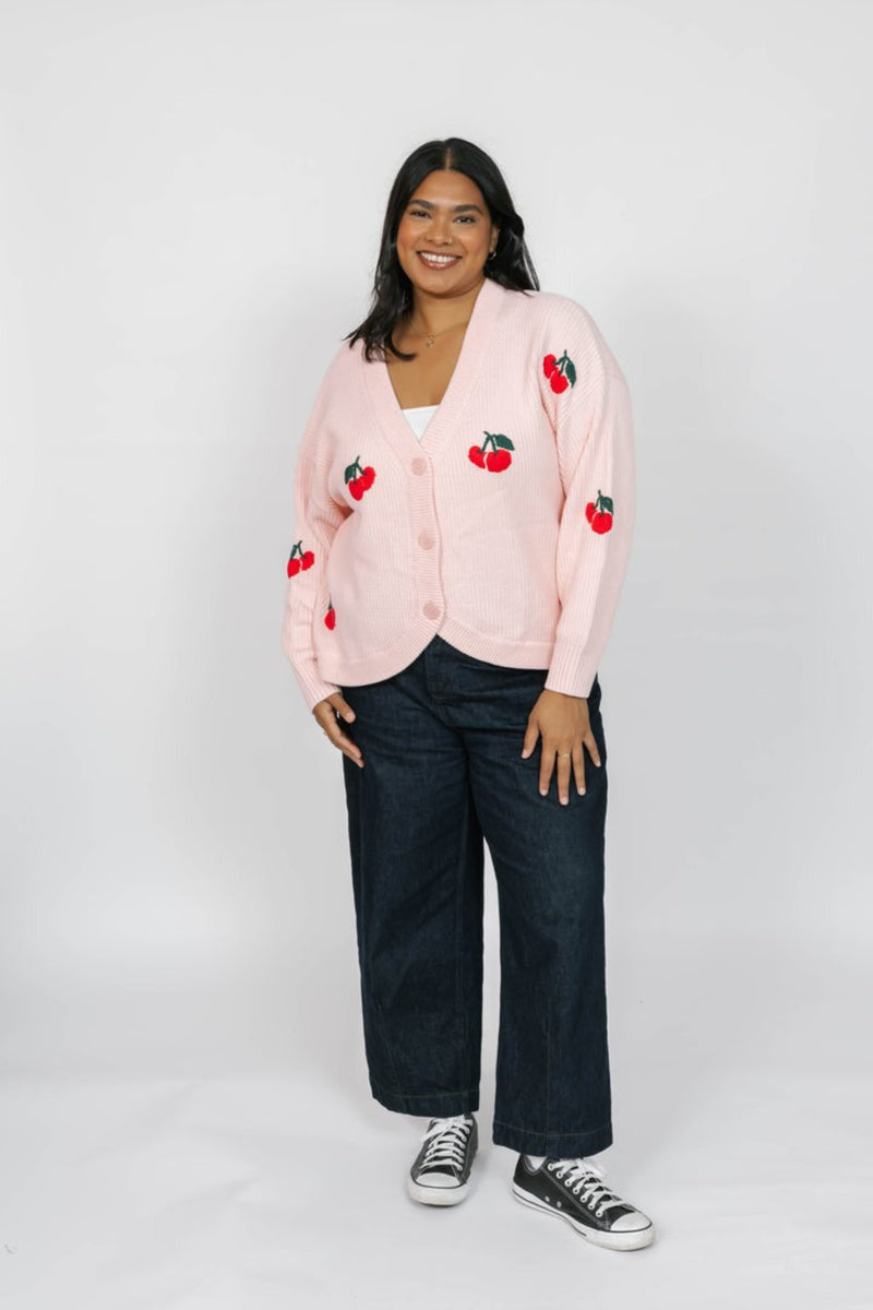 Person wearing a pink cardigan with cherry designs on a white background