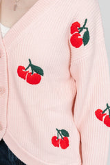 Pink cardigan with red cherry designs on a light gray background