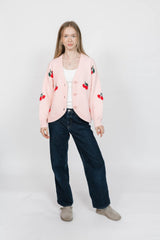 Person wearing a pink cardigan with red cherry patterns on a white background