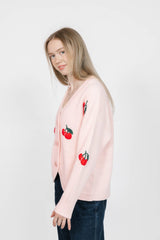 Woman wearing a light pink cardigan with red cherry designs on a white background
