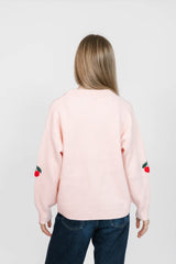 Person wearing a light pink sweater with cherry designs on a plain background