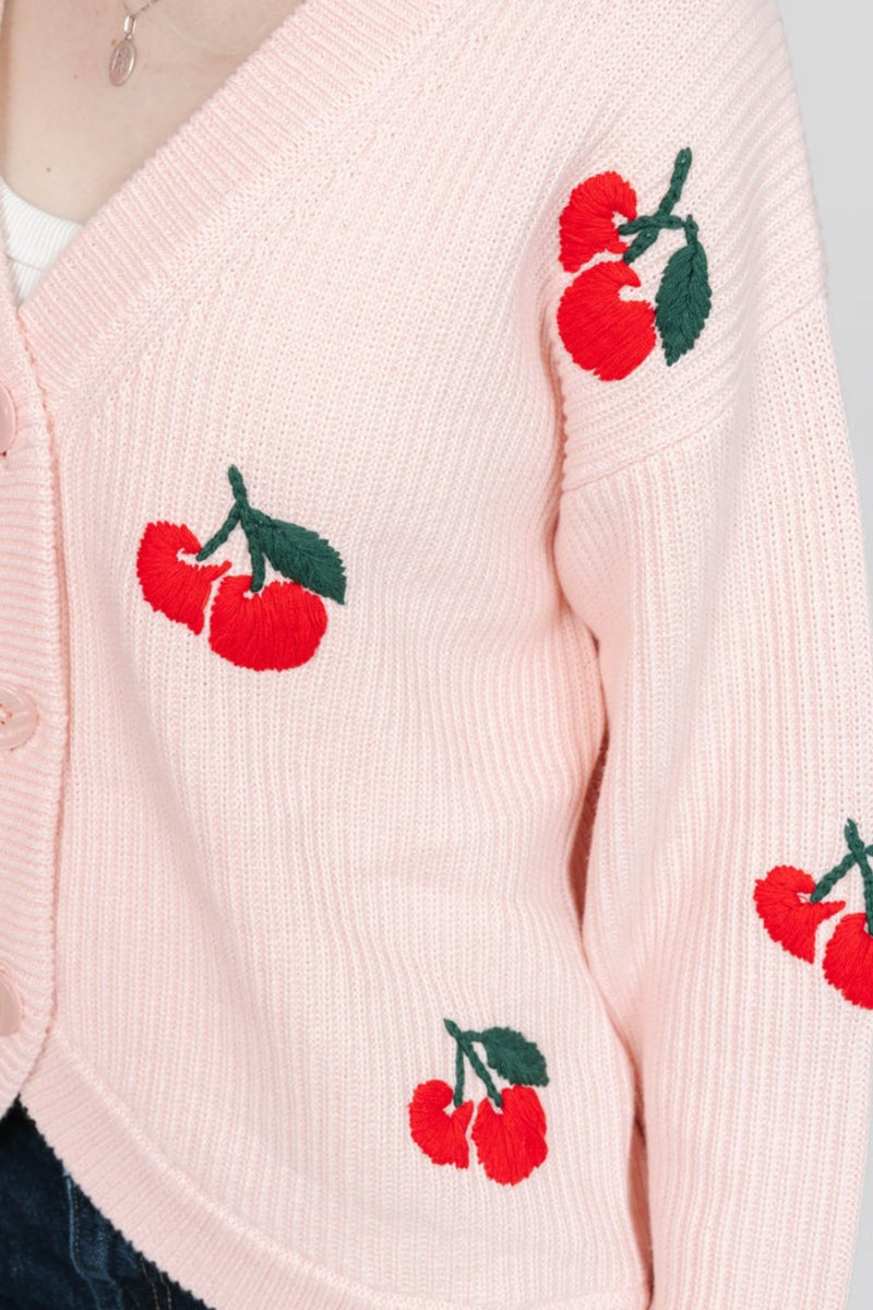 Pink cardigan with red cherry designs on a light gray background