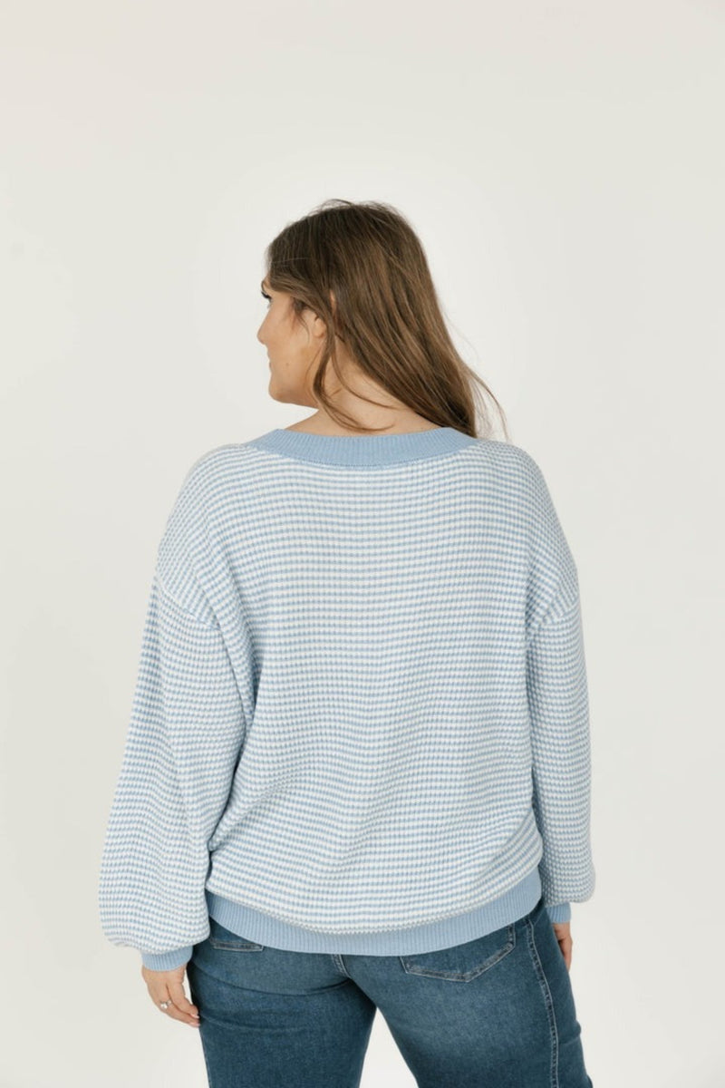 Woman wearing a light blue striped sweater and jeans on a white background