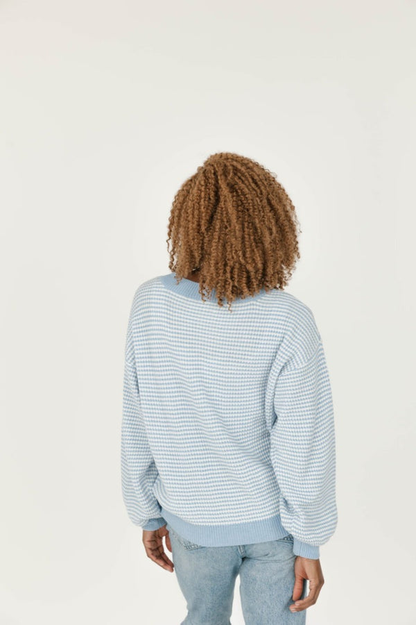 Person wearing a light blue striped sweater and jeans on a plain background