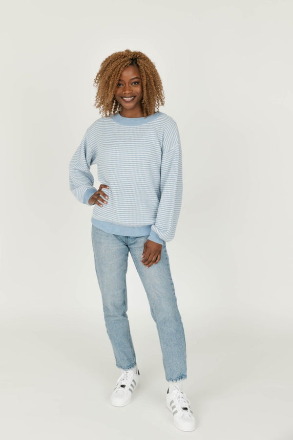 Person wearing a light blue striped sweater and jeans on a white background