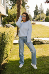 Woman posing outdoors in a suburban setting with greenery and a house in the background.