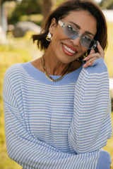 Woman wearing a blue and white striped sweater with sunglasses on a blurred outdoor background