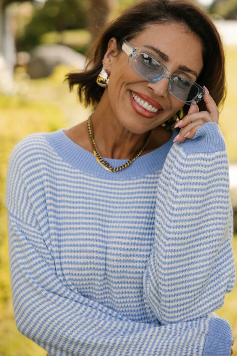Woman wearing a blue and white striped sweater with sunglasses on a blurred outdoor background
