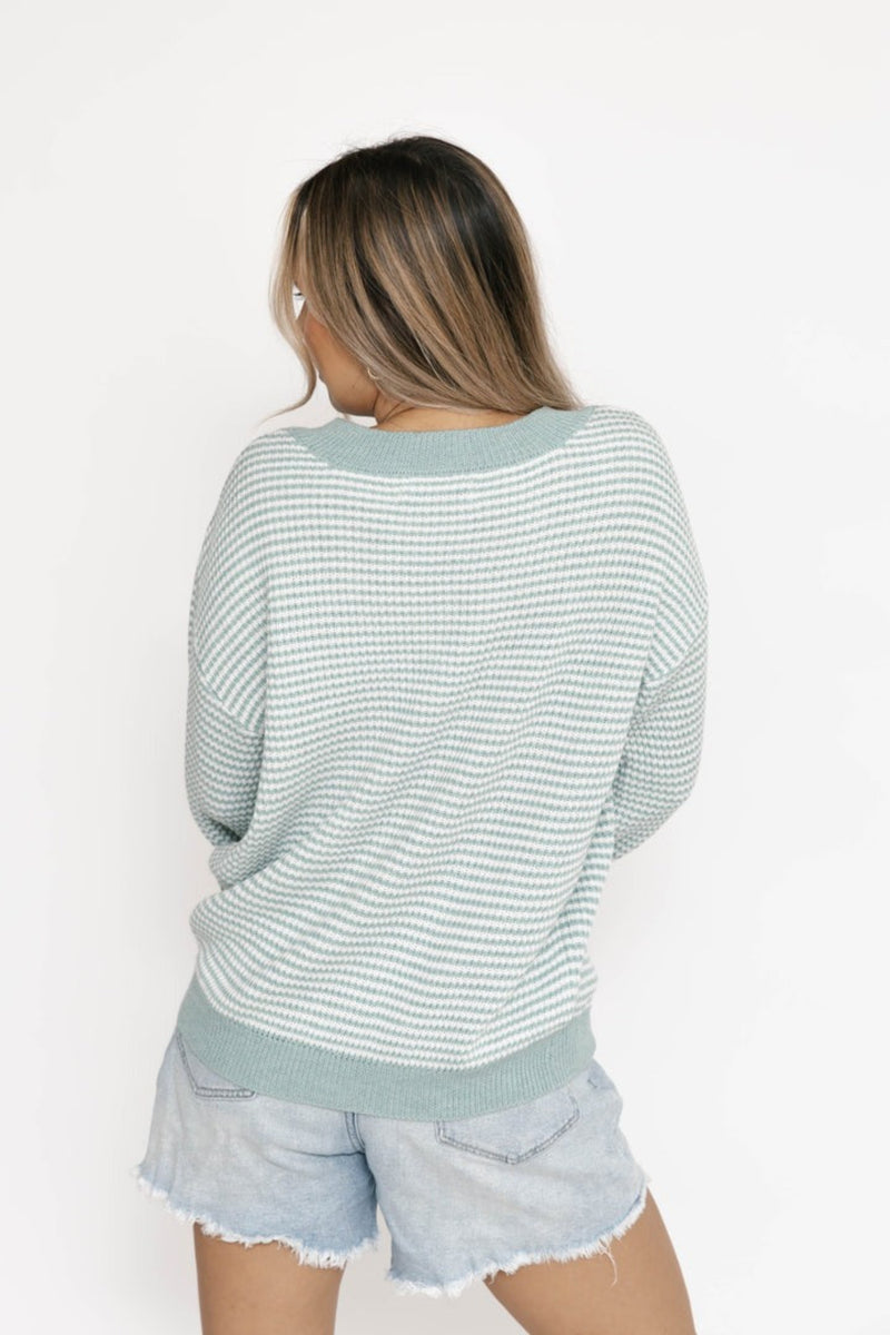 Woman wearing a light blue and white striped sweater and denim shorts on a white background