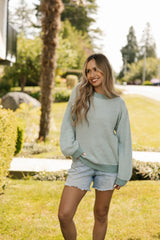 Woman wearing a green striped sweater and denim shorts standing in a park.