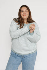 Woman wearing a light blue striped sweater and jeans on a white background