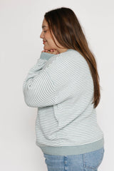 Woman wearing a light blue and white striped sweater against a plain background