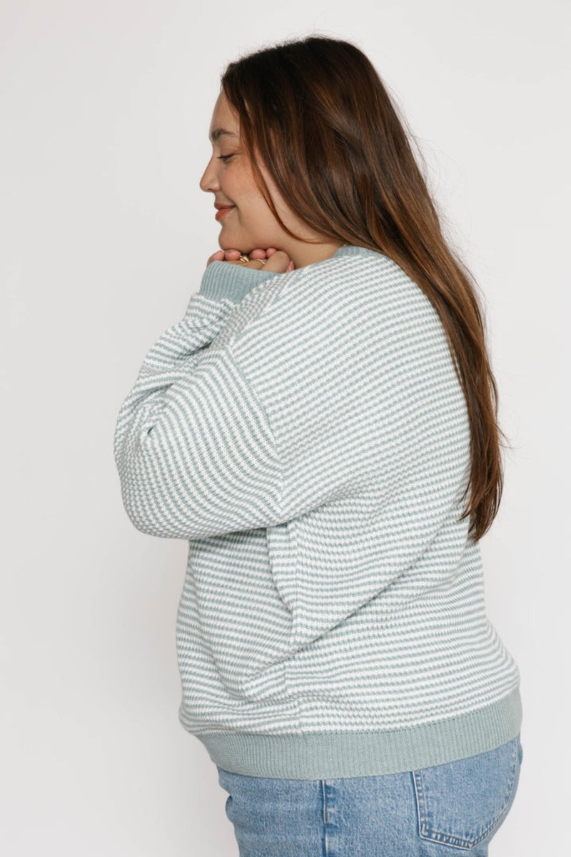 Woman wearing a light blue and white striped sweater against a plain background