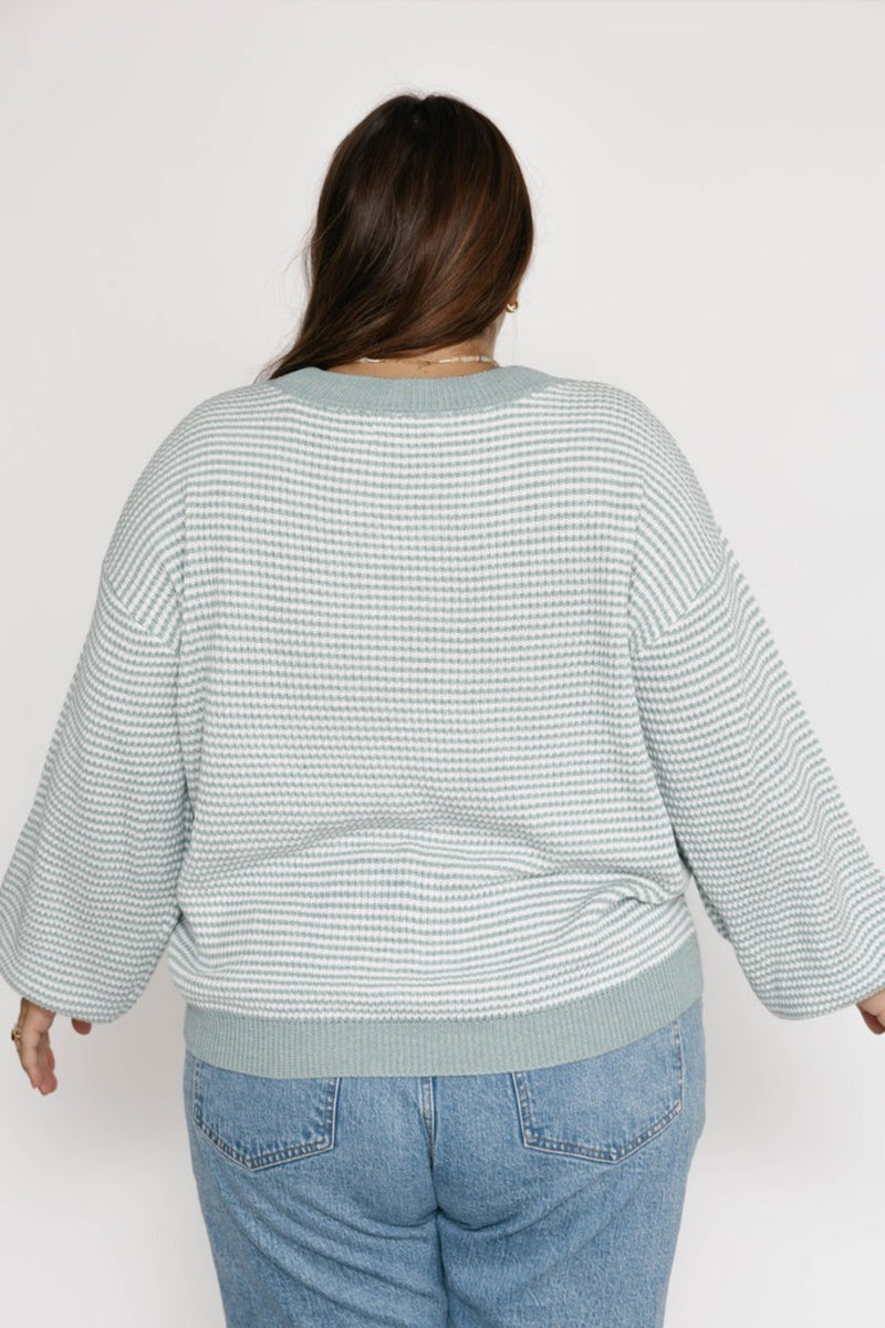 Person wearing a light blue striped sweater and jeans on a white background