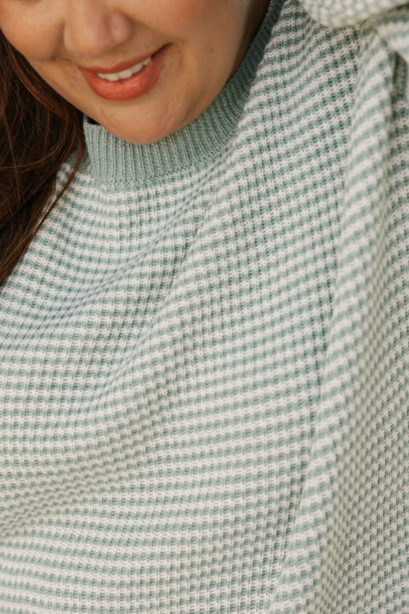 Close-up of a person wearing a textured green sweater with a blurred background