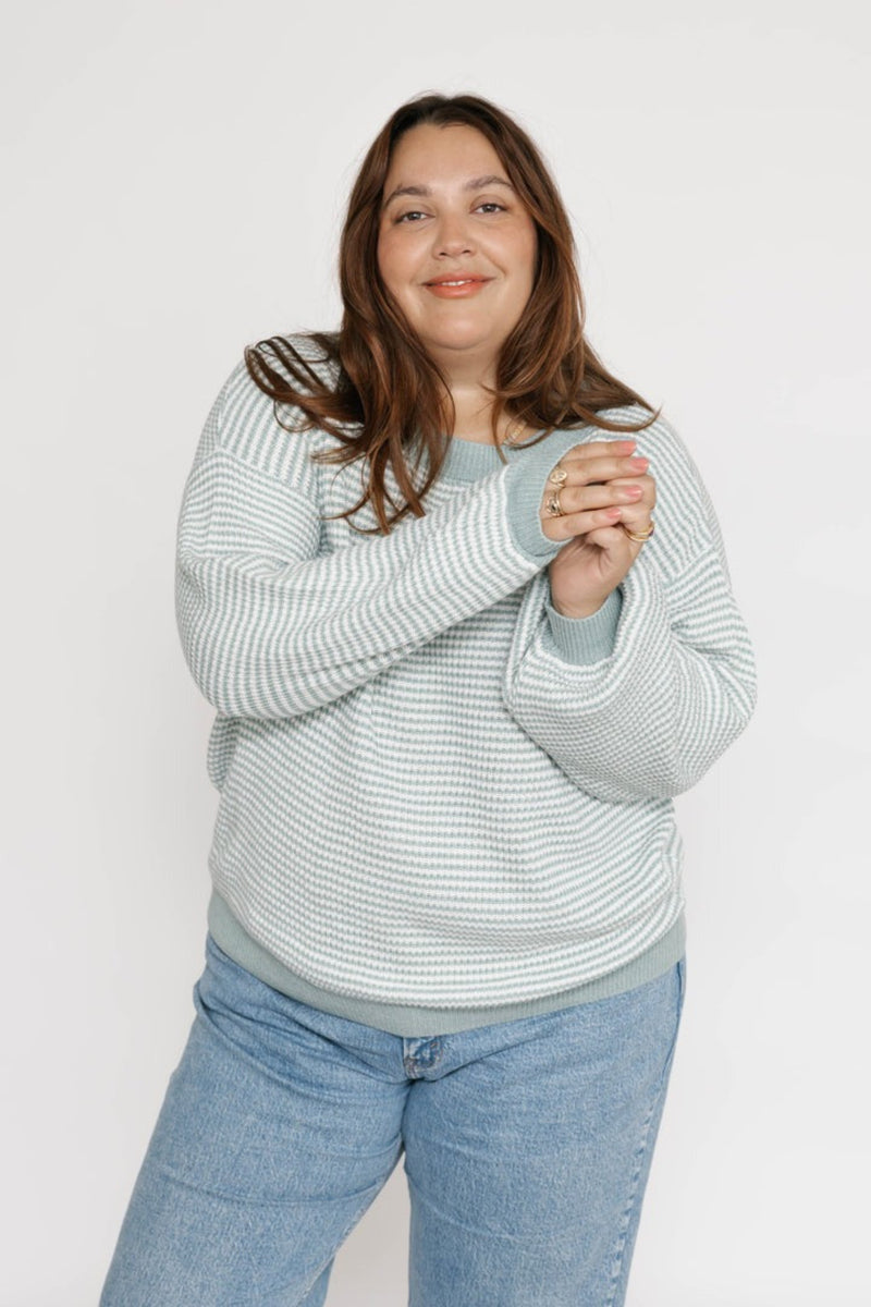 Woman wearing a light blue striped sweater and jeans on a white background