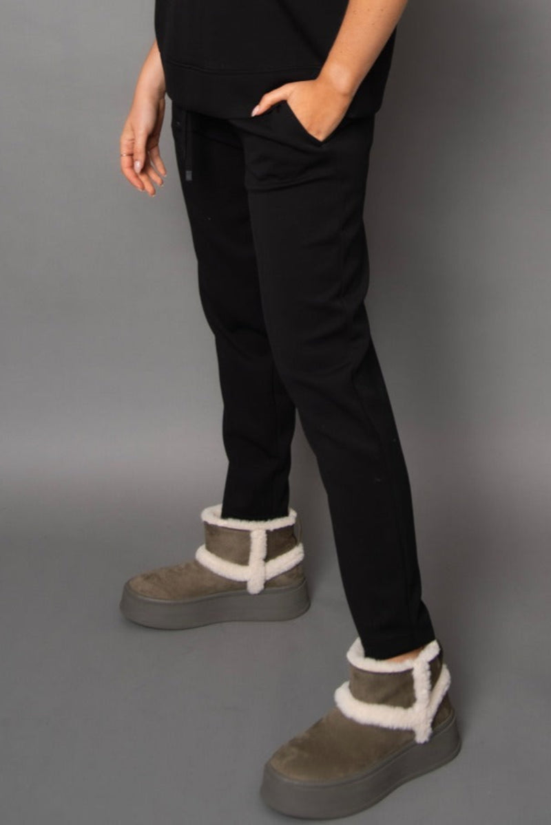 Person wearing black pants and brown boots with white fur trim on a gray background