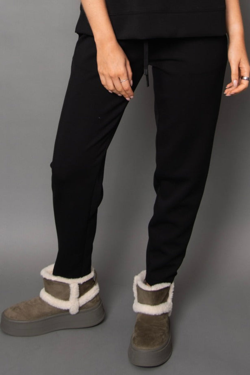 Person wearing black pants and brown boots with white fur trim on a gray background