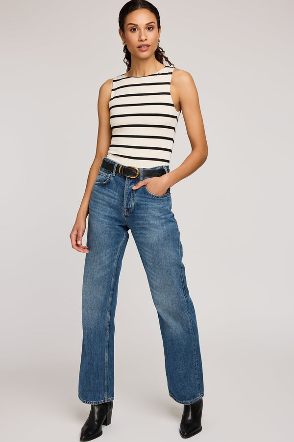Woman wearing a striped sleeveless top and blue jeans on a plain background