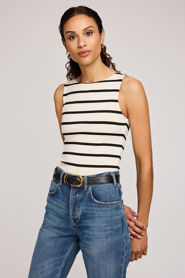 Woman wearing a black and white striped tank top and blue jeans on a plain background