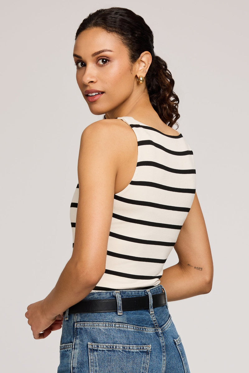 Woman wearing a black and white striped sleeveless top with blue jeans on a plain background