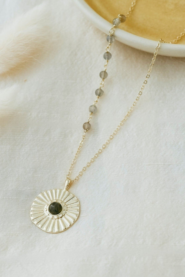Gold necklace with a circular pendant on a light fabric background
